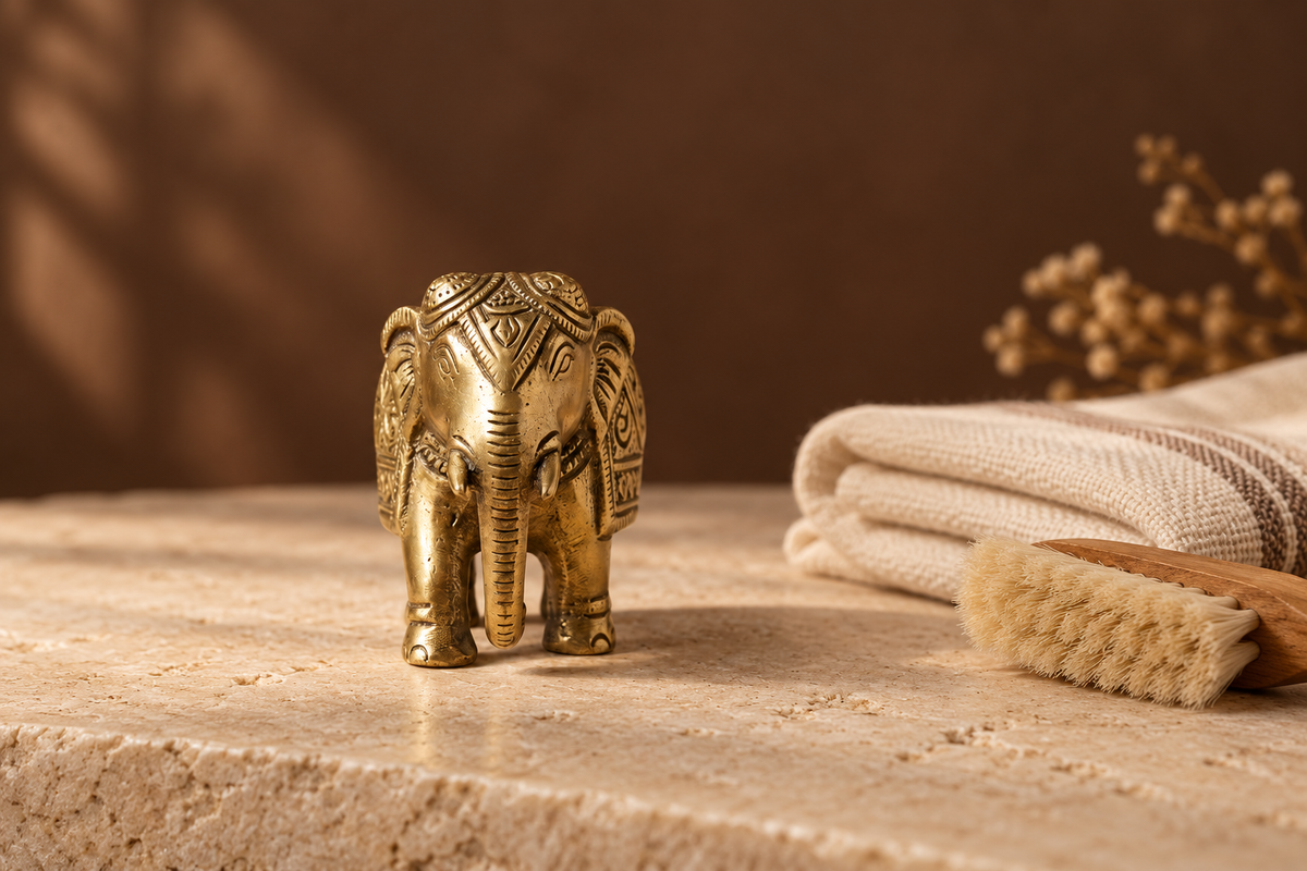 Antique-brass Ganesha idol beside a dry cotton cloth and soft brush on warm ivory stone