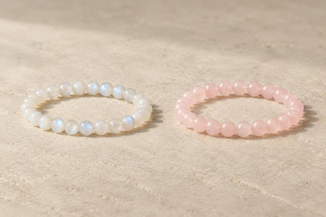 Editorial illustration of a pale moonstone bracelet beside a pink rose quartz bracelet on neutral stone.