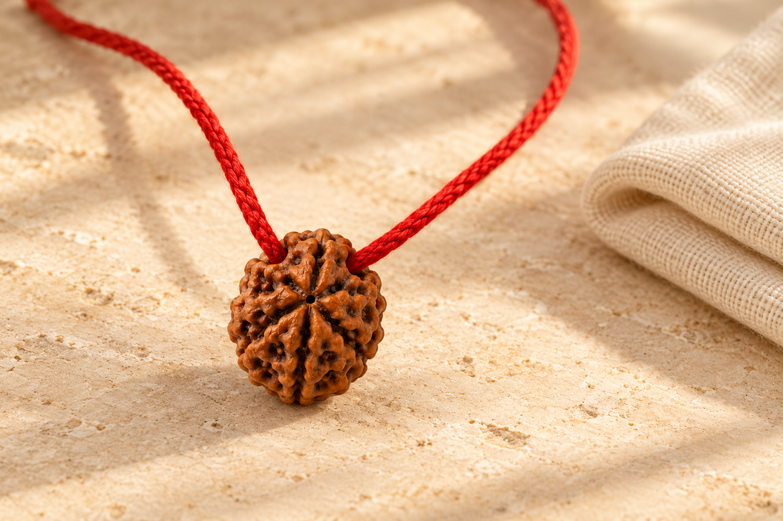 Seven Mukhi Rudraksha bead on a braided red thread beside a dry cotton cloth on warm ivory stone