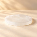 Round natural Selenite cleansing plate on a warm ivory background