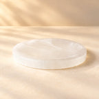 Round natural Selenite cleansing plate on a warm ivory background